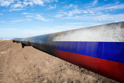 Long pipeline with Russian flag on dirt ground.
