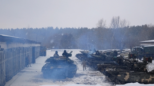 Tanks and soldiers in snowy setting near forest.