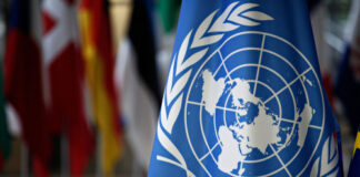United Nations flag with various country flags in background.