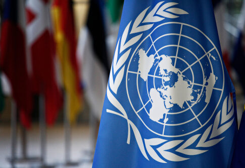 United Nations flag with various country flags in background.