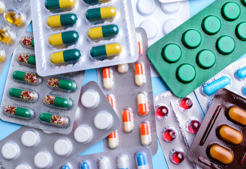 Various packs of colorful pills and capsules on blue background.