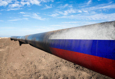 Long pipeline with Russian flag on dirt ground.