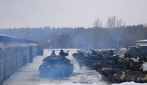 Tanks and soldiers in snowy setting near forest.