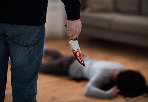 Person holding bloody knife with victim on the floor.