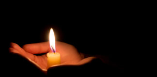 Hands holding a lit candle in darkness.