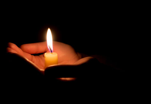 Hands holding a lit candle in darkness.