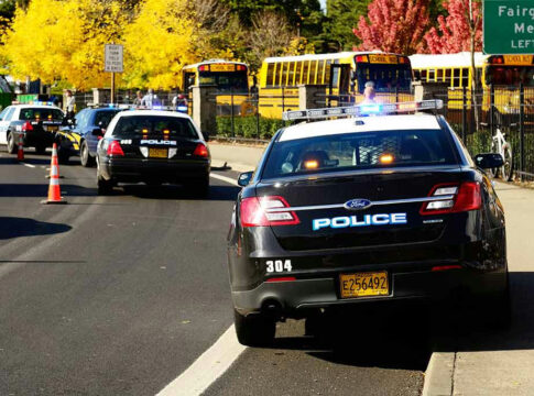Police cars and school buses on a sunny street.